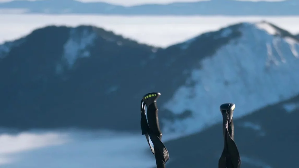 Bastoncini da trekking sopra un mare di nuvole, con le montagne innevate sullo sfondo